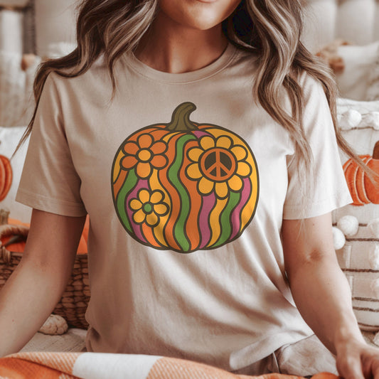Woman wearing a t-shirt with a colorful groovy retro pumpkin design in a cozy indoor setting with pumpkins and lights.