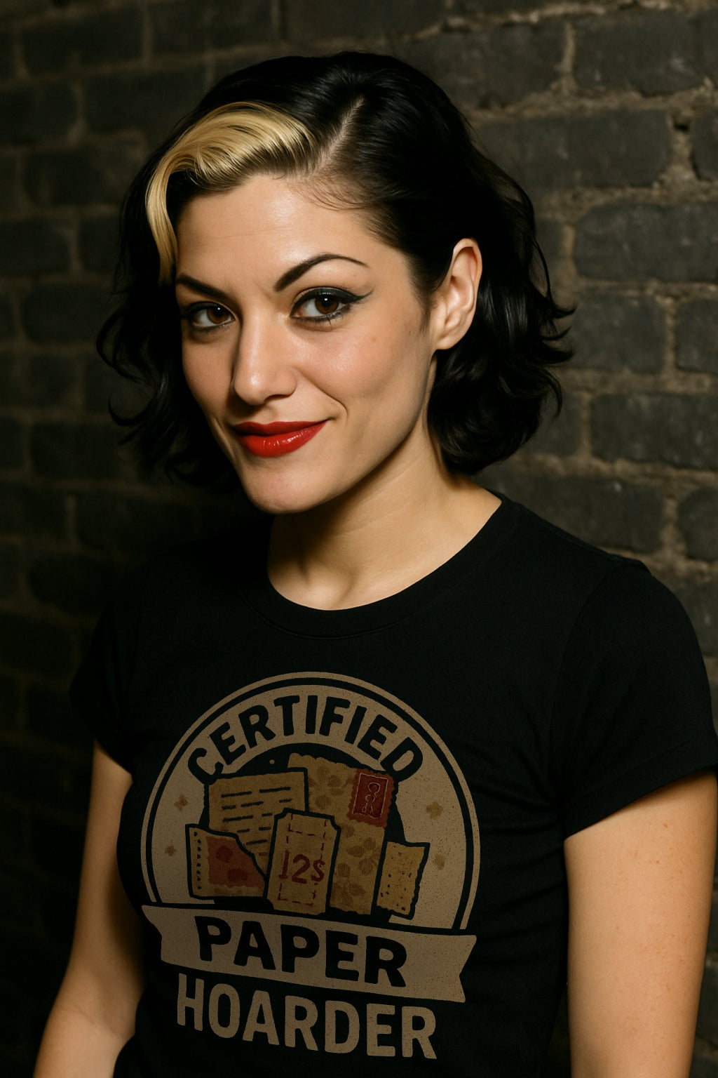 Woman wearing a black t-shirt with 'Certified Paper Hoarder' design, standing against a brick wall.