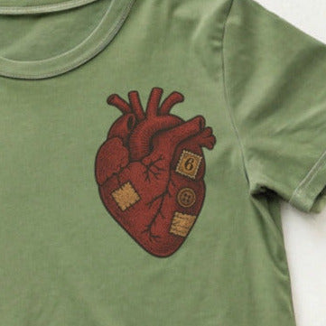 Green t-shirt with a patchwork heart design, blue jeans, and red sneakers on a white background