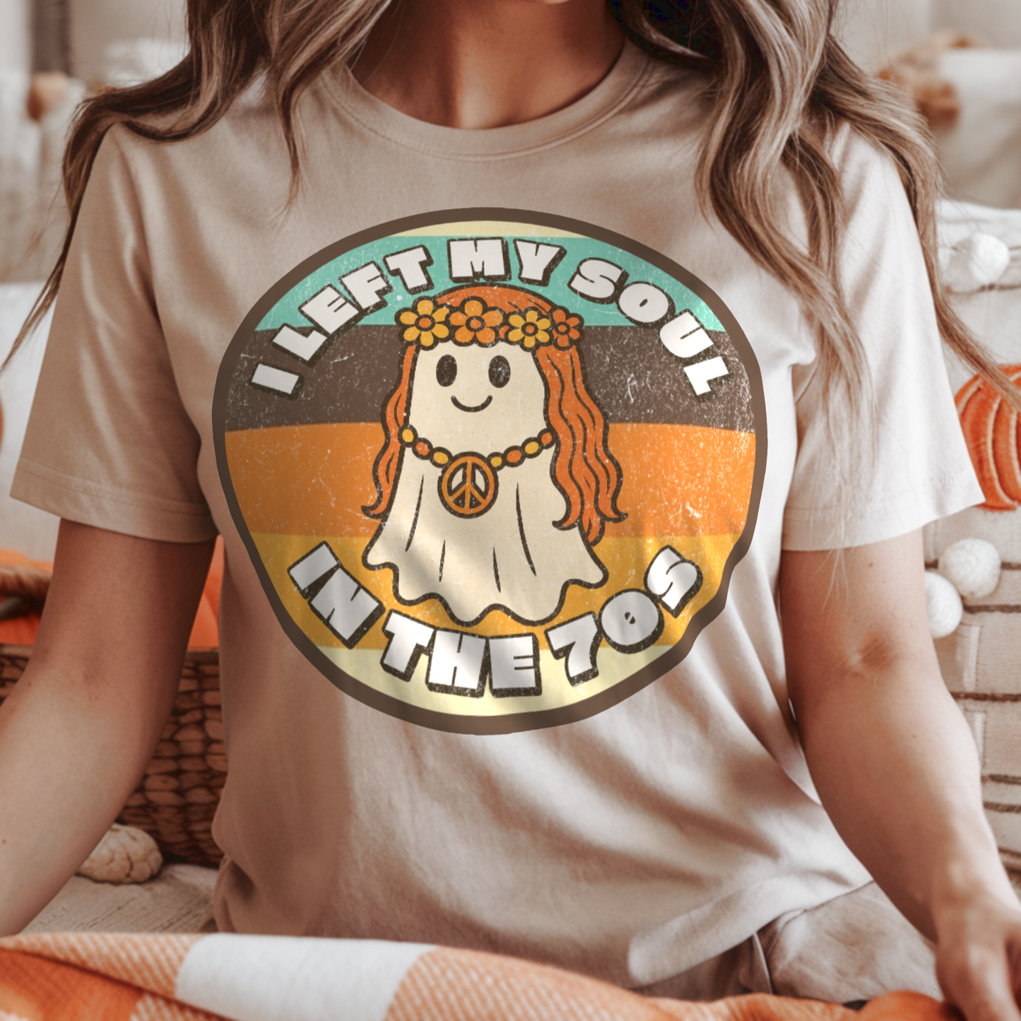 Person wearing a t-shirt with a 1970s flower child ghost design and text, sitting in a cozy room with pumpkins.