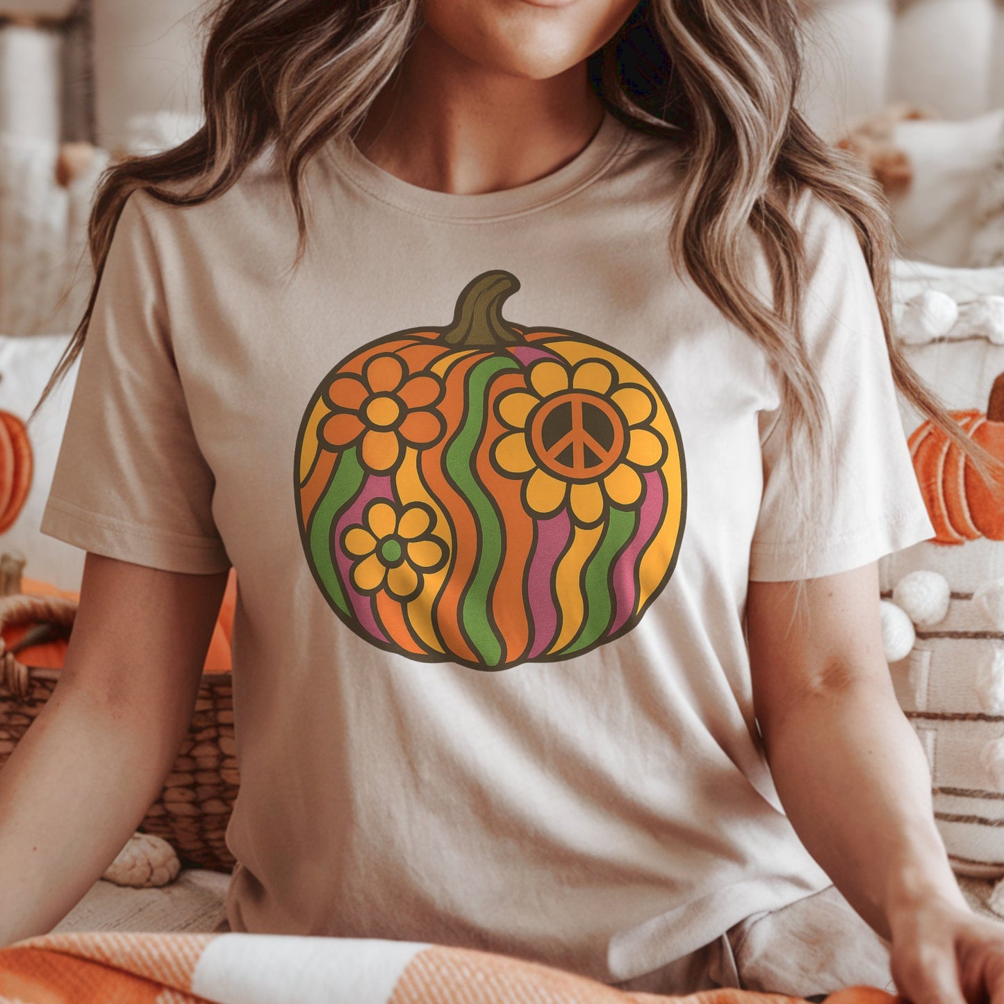 Woman wearing a t-shirt with a colorful groovy retro pumpkin design in a cozy indoor setting with pumpkins and lights.