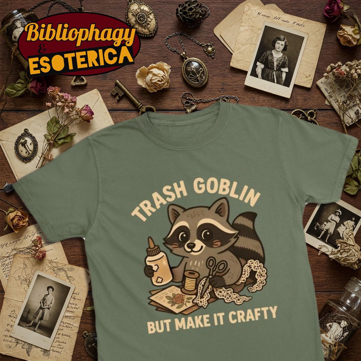 Green t-shirt with cute cartoon raccoon holding craft supplies and text 'Trash Goblin But Make It Crafty' on a vintage-themed background.