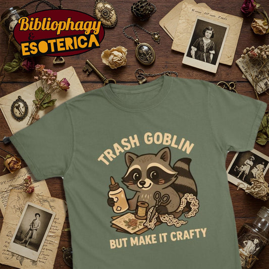 Green t-shirt with cute cartoon raccoon holding craft supplies and text 'Trash Goblin But Make It Crafty' on a vintage-themed background.